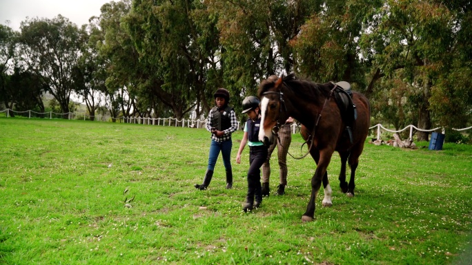 女教练和女孩在草地上遛棕马