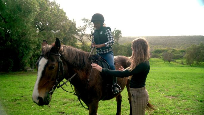 女教练在阳光明媚的田野里帮助女孩骑上棕马