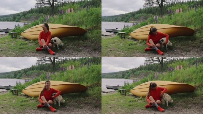 快乐的女性坐在黄色的独木舟旁，湖边的羽扇豆花抚摸着一只狗