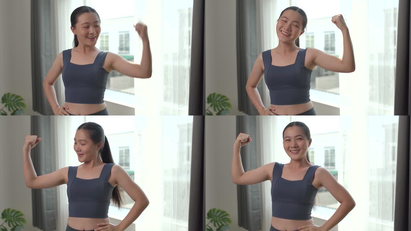 一位身穿运动服的亚洲女性在家中举起手臂，露出快乐的二头肌。