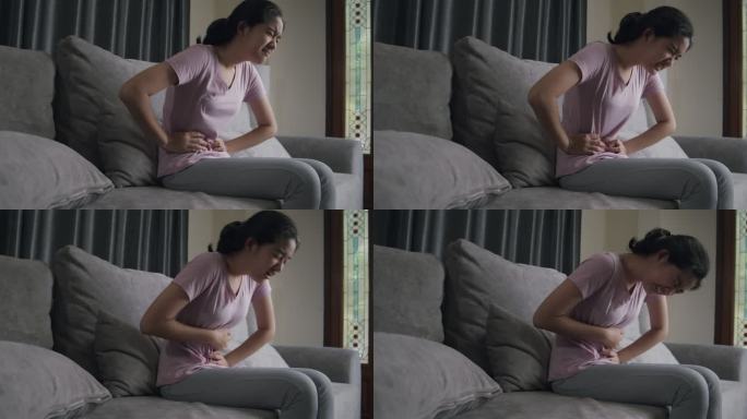 亚洲少女坐在家里的沙发上时骨盆疼痛胃痛