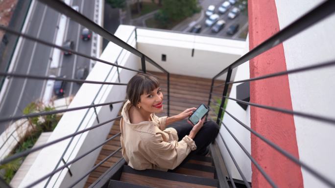 一名年轻女子坐在室外楼梯上使用智能手机的肖像