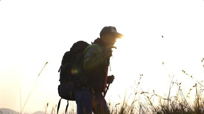 登山者迎着阳光正在负重前行爬山勇攀高峰