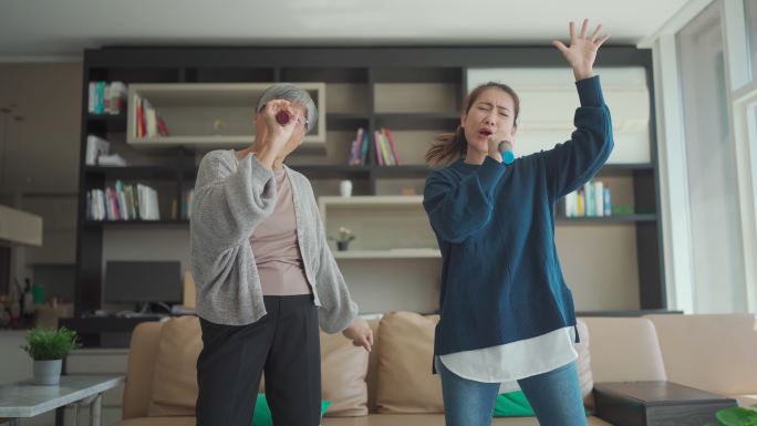 周末休闲活动期间，亚裔华裔老年妇女在客厅里和女儿一起唱卡拉ok跳舞