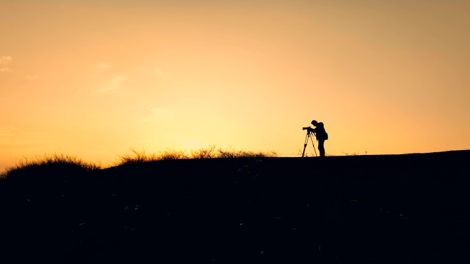 孤独的摄影人走在黄昏的山顶上
