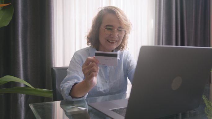 老年妇女用笔记本电脑上的信用卡在线支付药费