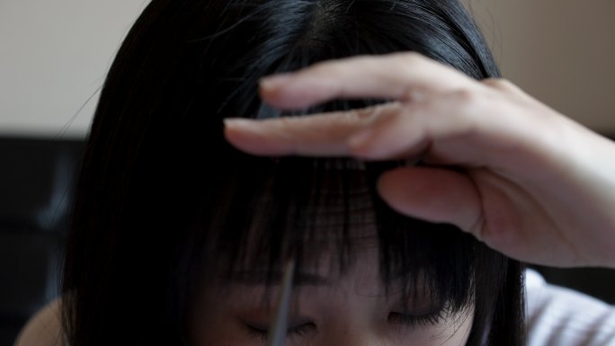 一位亚洲女性在家剪刘海。