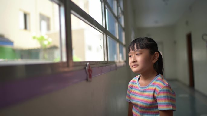沉思的女孩在学校透过窗户看