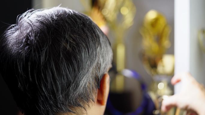 后视图：一位头发花白的男子正在整理他的获奖奖杯