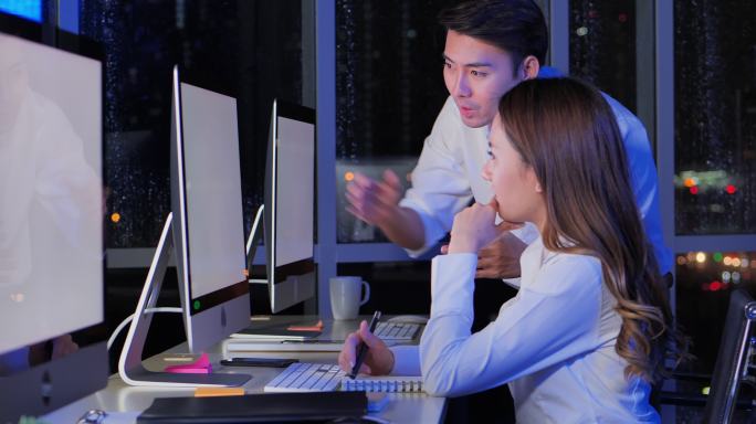在办公室里，领导亚洲的年轻男性对自信的女商人在深夜工作时一边用电脑分析数据，一边寻找解决方案。晚班概