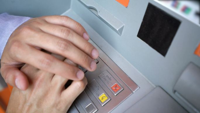 男性手在ATM机上用盖子输入pin码。