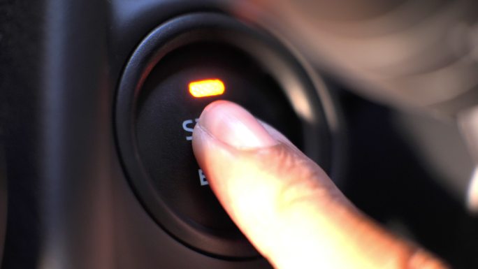 一个人在车里按下发动机启动按钮