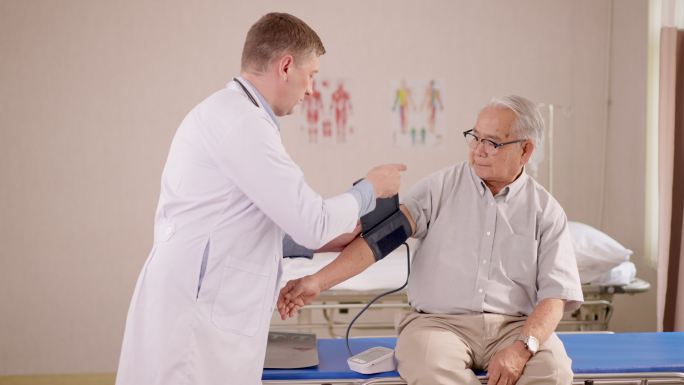 专业的男医生身穿白色实验室长袍，看着血压计，向坐在病床上的老年男性患者解释与心脏病和中风风险相关的结
