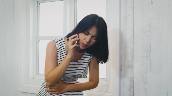 亚洲女性在客厅拿着手机，肚子疼