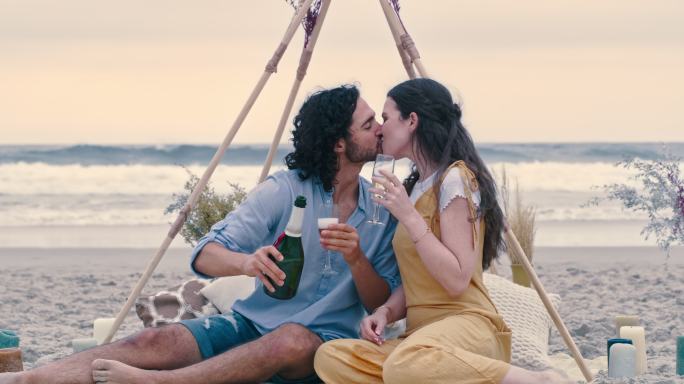 一对幸福的年轻夫妇在海滩上求婚后喝着香槟。一对年轻男女以酒吻和恋爱庆祝订婚