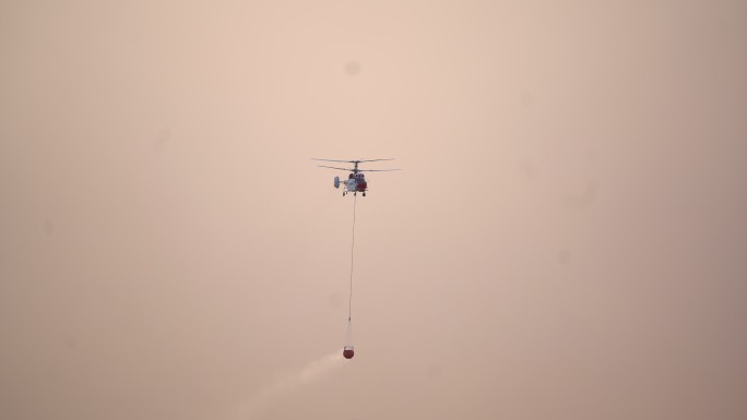 空中消防飞行直升机，在黄色多云的天空背景下带着水篮子。