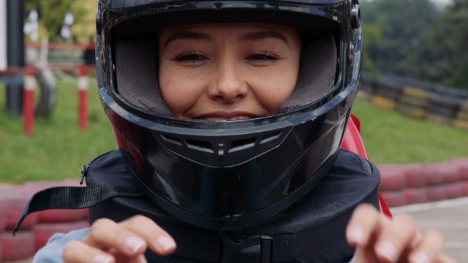 一个美丽快乐的女人在一个手推车赛道上面对镜头微笑时，确保头盔正确佩戴的视频肖像