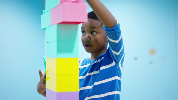 聚焦于非洲黑人儿童，一个7岁的男孩在客厅里享受并打算连接高达头顶的彩色塑料积木。