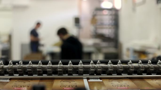 当工人在后台工作时，一台自动化机器正在印刷厂堆叠印刷介质