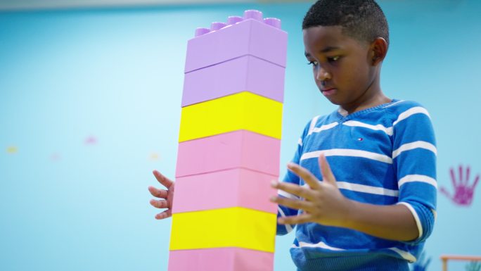 非洲黑人儿童，一个7岁的男孩试图将五颜六色的塑料积木尽可能高地连接起来，同时他需要意识到并保护建筑积