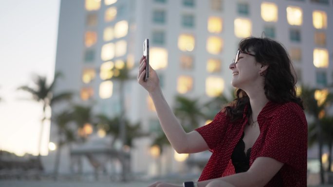 女子坐在酒店附近的海滩上通过智能手机进行视频通话