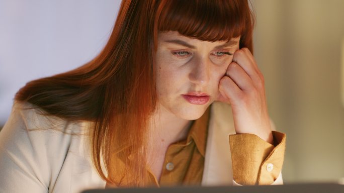 一位疲惫的女商人在现代办公室深夜使用笔记本电脑。一位压力很大的年轻商业女性，在网上用电脑工作