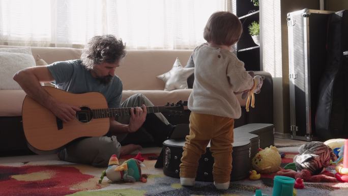 成熟的父亲在家照顾女儿时弹吉他。