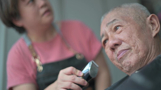 白天在家前院车库的轮椅上为父亲理发的亚裔中国妇女