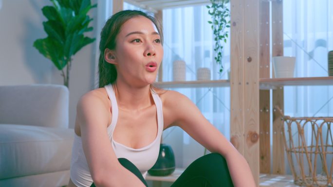 亚洲年轻的运动女性在做有氧运动后休息并深呼吸。穿着运动服的漂亮女孩在起居室里利用垫子进行休闲锻炼，以