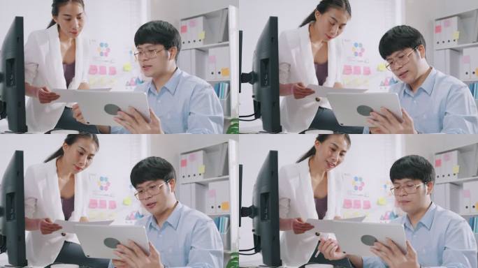 年轻的亚洲商人坐在电脑桌前，看着数字平板电脑的书写，在小工作场所为他的女同事检查工作报告、营销和演示