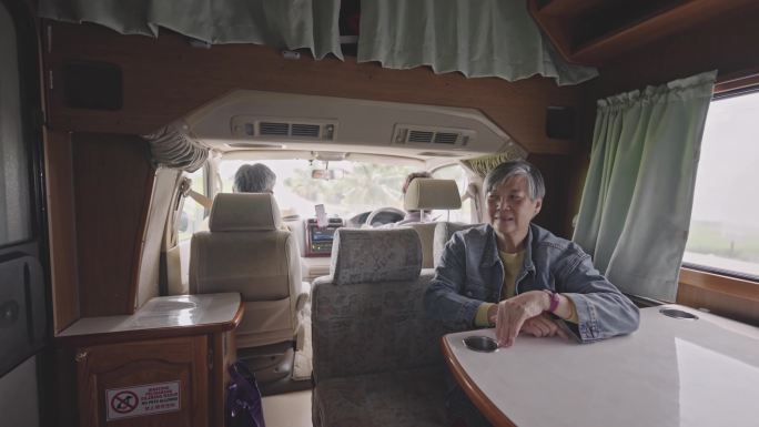 一位亚裔中国资深女性坐在汽车后座欣赏乡村风光时与朋友交谈