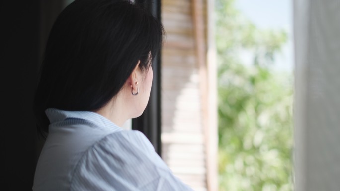 亚洲女子拉开窗帘，走到海滨度假阳台眺望风景