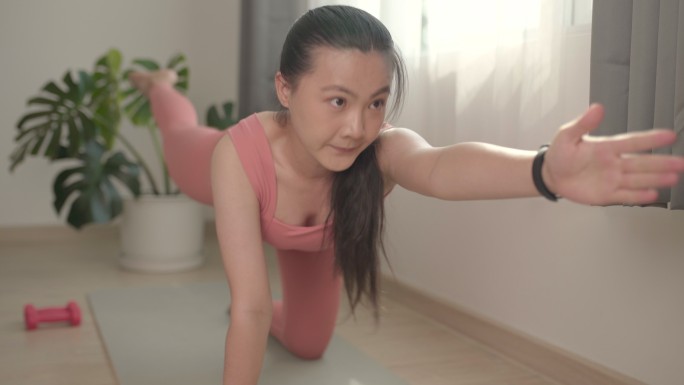 一位穿着运动服的亚洲女性在家里的垫子上锻炼，同时在网上观看视频博客。