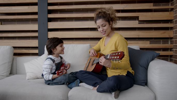 美丽的年轻妈妈和她的儿子一起弹吉他，笑着唱歌都很开心