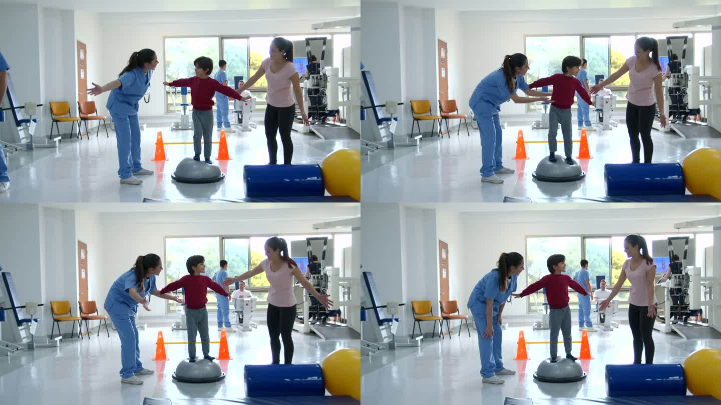 在物理治疗期间，一个可爱的小男孩按照治疗师和妈妈的指示，试图站在锻炼的半边球上