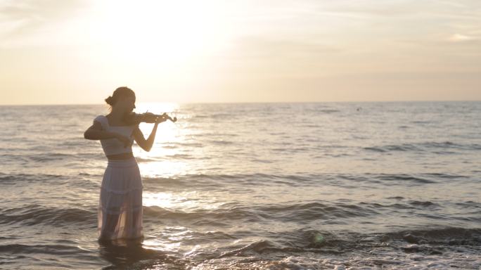 日落时分，十几岁的女孩在海滩上拉小提琴
