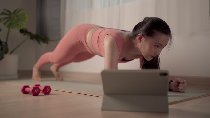 一位穿着运动服的亚洲女性在家里的垫子上锻炼，同时在网上观看视频博客。