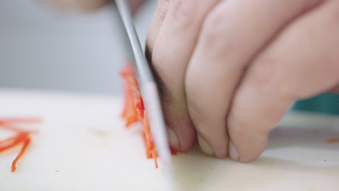厨师用锋利的菜刀将红辣椒切成薄片。