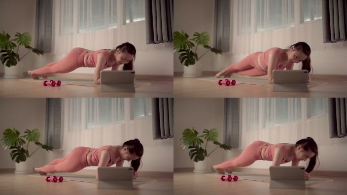 一位穿着运动服的亚洲女性在家里的垫子上锻炼，同时在网上观看视频博客。慢动作视频。
