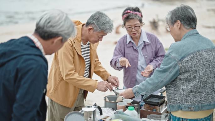 周末休闲活动期间，亚洲的中国老年朋友在停在海滩上的露营车旁准备早餐