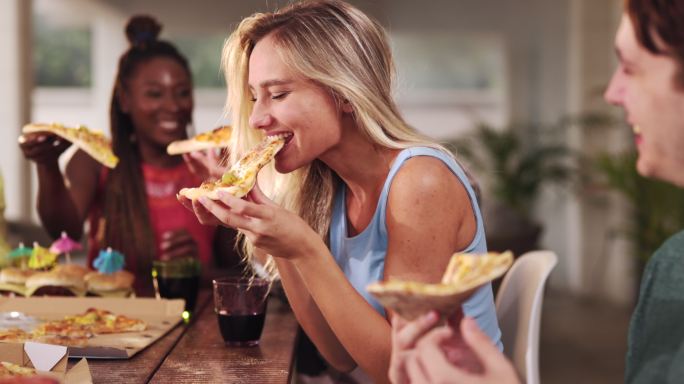 快乐的年轻女人和她的朋友一起吃披萨。