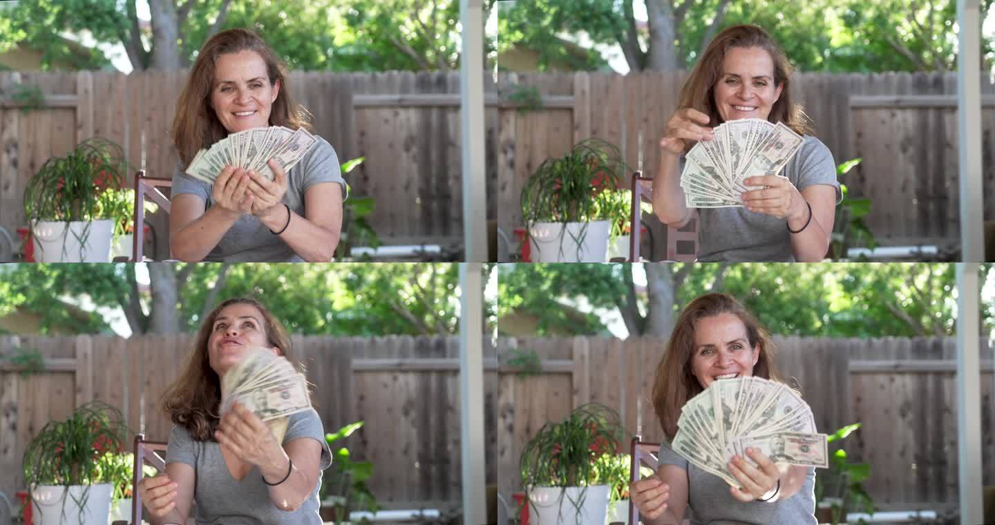 微笑的成熟女人拿着一堆美元钞票坐在后院