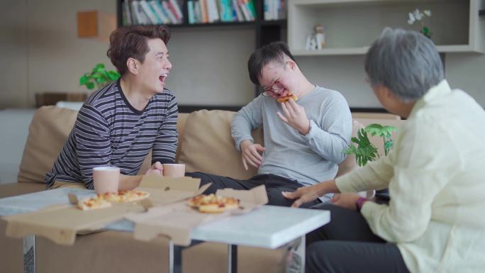 亚洲中国多代唐氏综合征家庭的孙子周末坐在沙发上在客厅享受披萨快餐