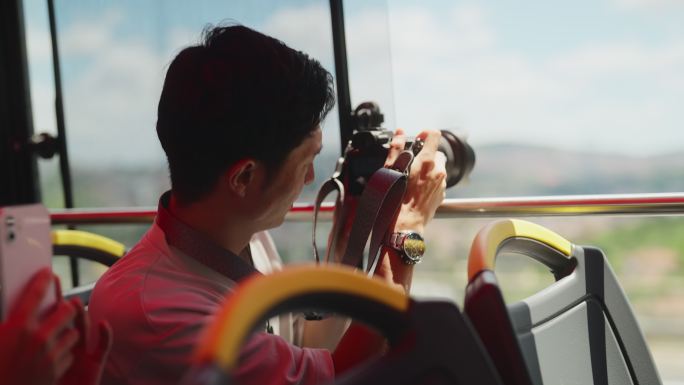 年轻的男性游客乘坐城市旅游巴士，并在旅行中拍摄照片和视频