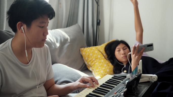 亚洲男孩在家里靠窗的沙发上通过手机应用程序学习键盘乐器，生活方式理念。