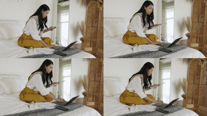 年轻的亚洲女性坐在房间的床上用智能手机在线支付