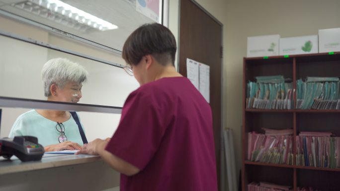 亚洲华人老年女性用信用卡支付医疗账单点击诊所女护士持有的信用卡读取器NFT