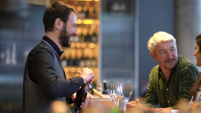 在品酒会上，一对幸福的夫妇在专业品酒师微笑着打开葡萄酒时与他交谈