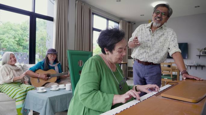 一群老年朋友喜欢在客厅里一起弹钢琴和唱歌，亚洲老年朋友在家里聚会