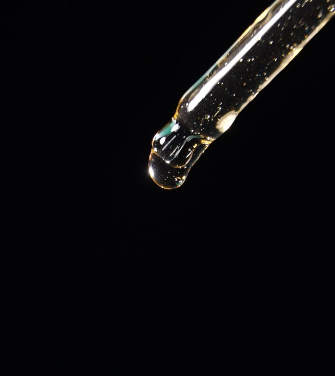 垂直拍摄：油滴从黑色背景的移液管中滴落